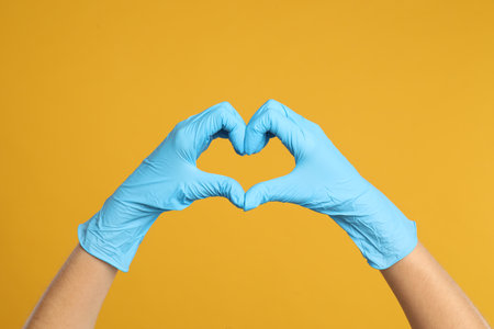 Doctor in medical gloves showing heart with hands on yellow background, closeupの写真素材