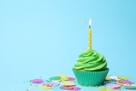 Delicious birthday cupcake with green cream and burning candle on light blue background. Space for textの写真素材