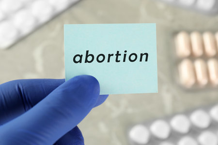 Doctor holding paper card with word ABORTION over table with pills, closeupの写真素材