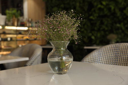 Glass vase with bouquet of beautiful flowers on table in cafeの写真素材