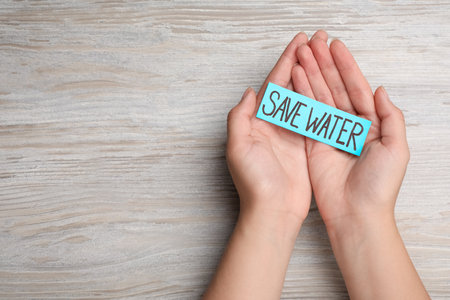 Woman holding card with words Save Water on wooden background, top view. Space for textの写真素材