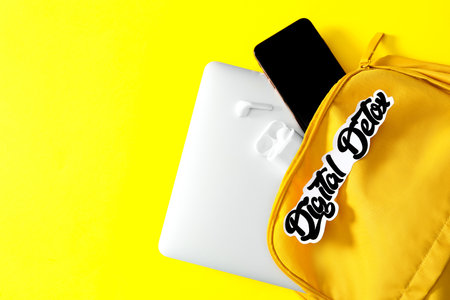 Different gadgets in bag with words DIGITAL DETOX on yellow background, flat lay. Space for textの写真素材