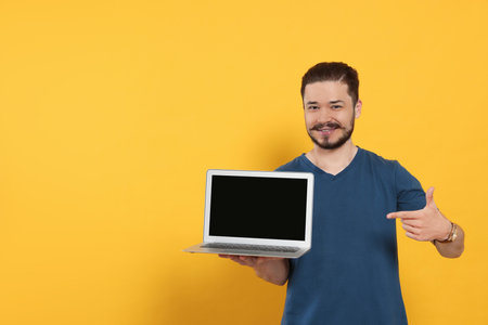 Emotional man pointing at laptop on orange background. Space for textの写真素材