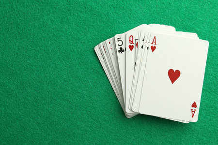 Deck of playing cards on green table, top view. Space for text