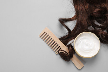 Lock of healthy brown hair, comb and cosmetic product on light gray background, flat lay. Space for textの写真素材
