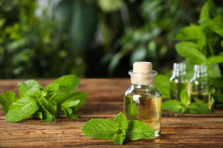Bottle of mint essential oil and green leaves on wooden table, space for textの写真素材