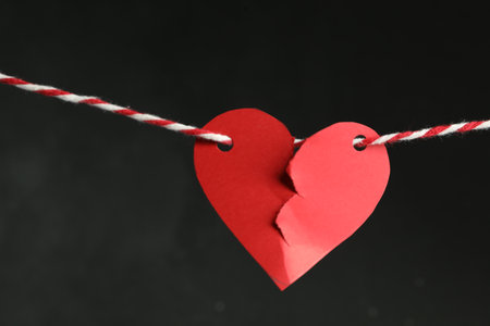 Broken red paper heart on rope against black background. Relationship problems conceptの写真素材