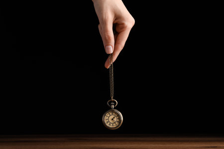 Psychotherapist with pendulum on black background, closeup. Hypnotherapy sessions