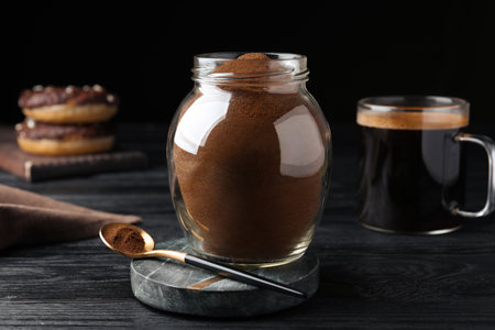 Jar of instant coffee and spoon on black wooden tableの写真素材