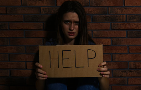 Abused young woman with sign HELP near brick wall. domestic violence conceptの写真素材