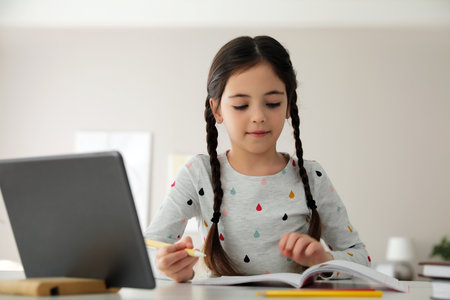 Little girl doing homework with modern tablet at homeの写真素材
