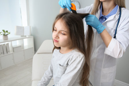 Doctor using nit comb on girl's hair in clinic. Anti-lice treatment