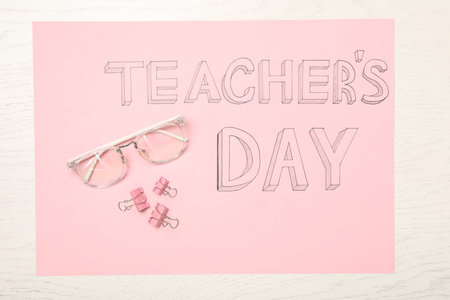 Sheet of pink paper with words TEACHER'S DAY, glasses and clips on white wooden background, top viewの写真素材