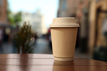 Cardboard takeaway coffee cup with lid on wooden table in city, space for textの写真素材