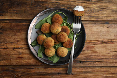 Delicious falafel balls with spinach and sauce on wooden table, top view