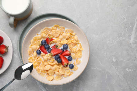 Bowl of tasty crispy corn flakes with milk and berries on light gray table, flat lay. Space for text