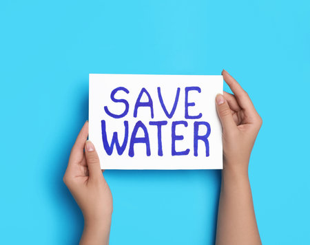 Woman holding card with words Save Water on light blue background, top viewの写真素材