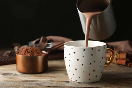 Pouring hot cocoa drink into cup on wooden tableの写真素材