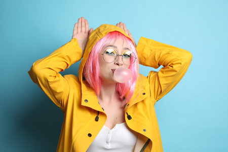 Fashionable young woman in pink wig with bright makeup blowing bubblegum on yellow backgroundの写真素材