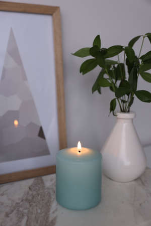 Beautiful burning candle and vase with green branches on marble tableの写真素材