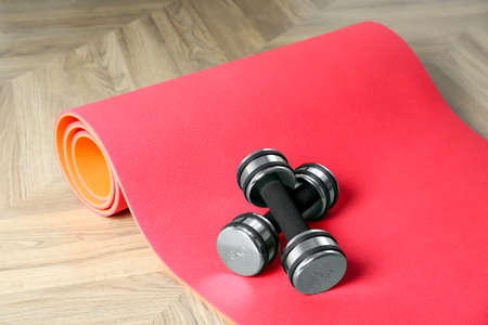 Exercise mat and dumbbells on wooden floor indoors