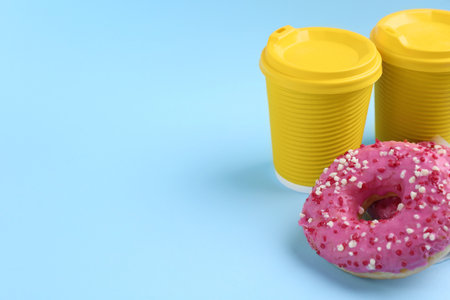 Delicious fresh donuts with sprinkles and hot drink in paper cups on light blue background, space for textの写真素材