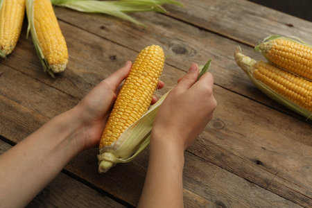 Woman husking corn cob at wooden table, closeup