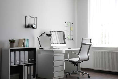 Comfortable white chair near desk in stylish office interiorの写真素材