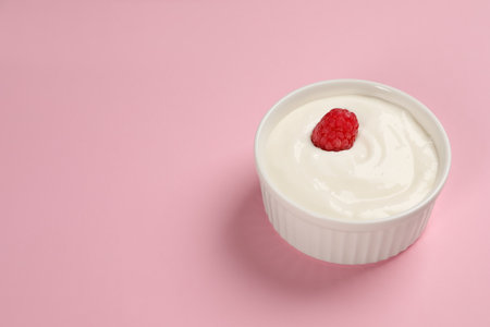 Tasty yogurt with raspberry in bowl on pink background, space for textの写真素材