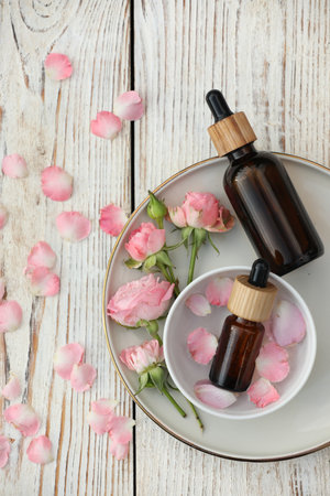 Bottles of rose essential oil and flowers on white wooden table, flat layの写真素材