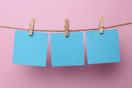 Wooden clothespins with blank notepapers on twine against pink background. Space for textの写真素材