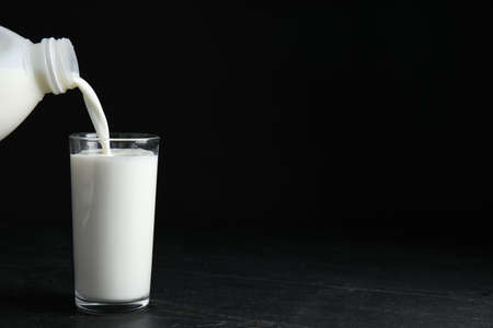 Pouring milk from gallon bottle into glass on black table. Space for text