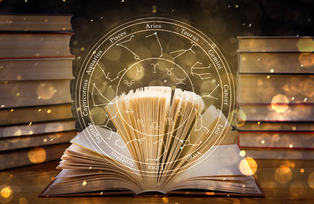Open book on wooden table and illustration of zodiac wheel with astrological signsの写真素材
