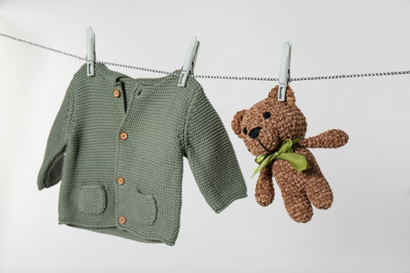 Baby shirt and toy bear drying on laundry line against light backgroundの写真素材