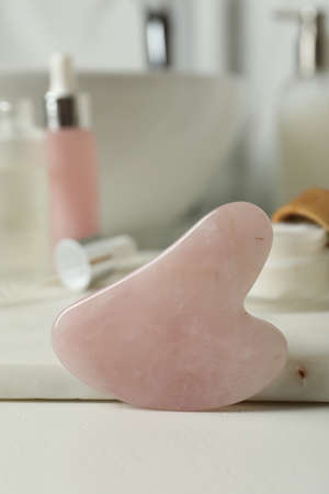 Rose quartz gua sha tool and toiletries on white countertop in bathroom, closeupの写真素材