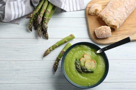 Delicious asparagus soup in bowl on white wooden table, flat layの写真素材