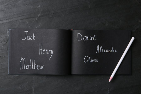 Notebook with written different baby names and pencil on black table, flat layの写真素材
