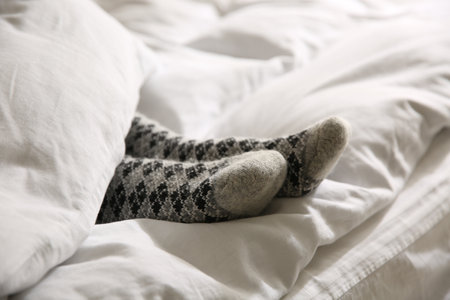 Woman wearing knitted socks under blanket in bed, closeupの写真素材