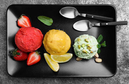 Strawberry, lemon and pistachio ice cream scoops served on gray table, top view