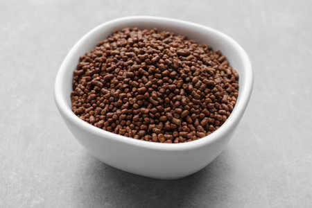 Buckwheat tea granules in bowl on light gray table, closeup