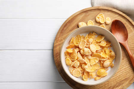 Tasty cornflakes with milk served on white wooden table, top view. Space for text