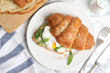 Delicious croissant with arugula and egg on white marble table, flat layの写真素材