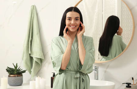 Beautiful young woman near mirror in bathroom