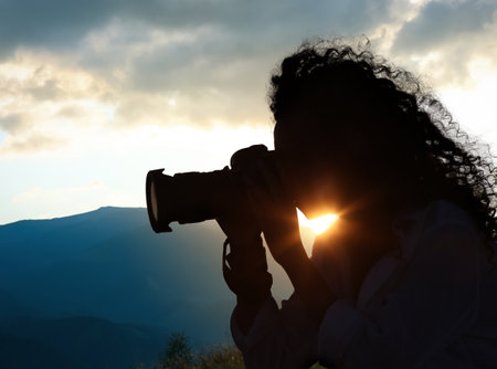 Photographer taking picture of beautiful mountains at sunset with professional cameraの写真素材