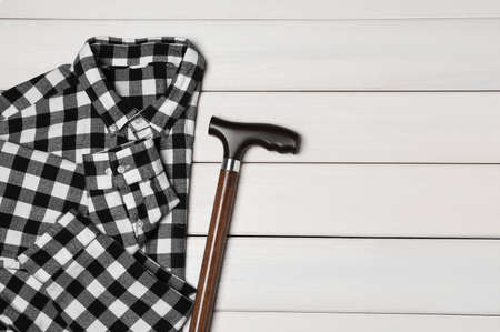 Elegant walking cane and checkered shirt on white wooden table, flat lay. Space for textの写真素材