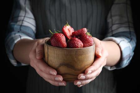 Woman holding bowl with tasty fresh strawberries on black background, closeup