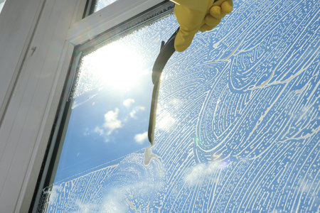 Woman cleaning glass with squeegee indoors, closeup
