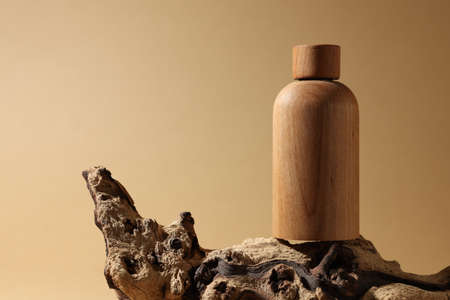 Wooden bottle of cosmetic product on tree bark against dark beige background, space for textの写真素材