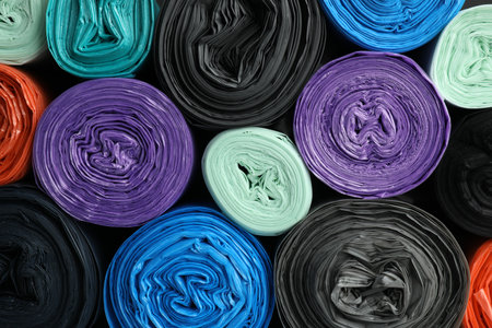 Rolls of different color garbage bags as background, top view