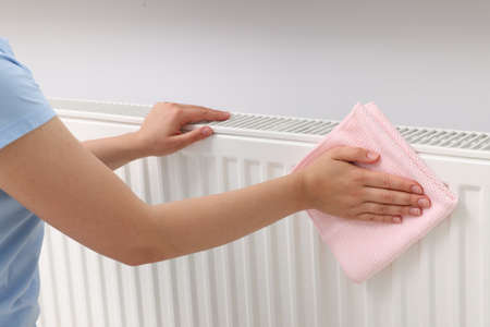 Woman cleaning radiator with rag indoors, closeupの写真素材